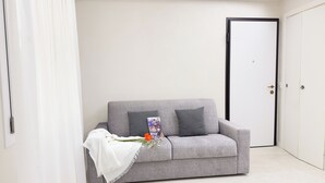 Ein graues Sofa mit weißer Decke und einem dekorativen Gegenstand, eine weiße Tür sowie eine weiße Wand.