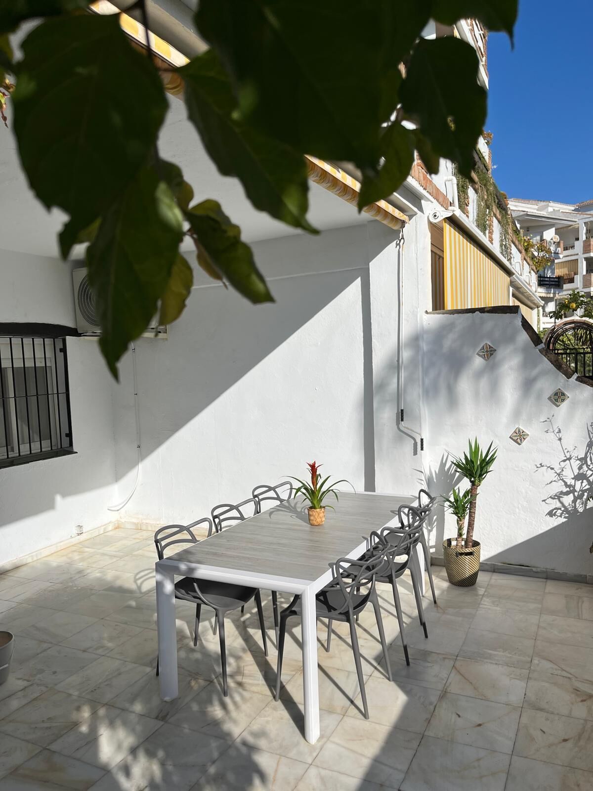 Eine sonnendurchflutete Terrasse mit einem weißen Tisch und Stühlen, umgeben von weißen Wänden und einem gefliesten Boden.