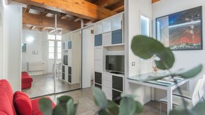 A modern living room with a glass dining table, red sofa, and a TV on a white cabinet. - Domus 2 in Como by Rent All Como (Como)