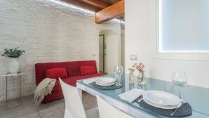 A modern living room with a red sofa, a glass dining table set with plates and wine glasses, and a white brick wall. - Domus 2 in Como by Rent All Como (Como)