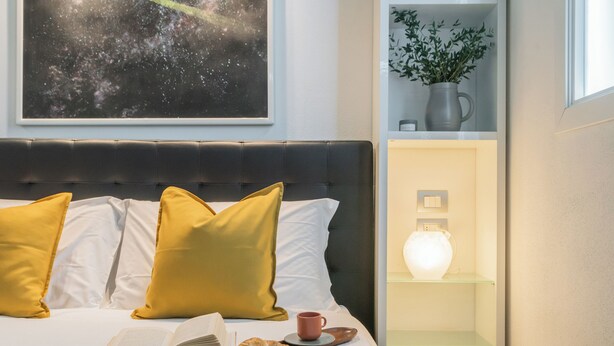 A neatly made bed with yellow pillows, a book, and a croissant on a tray. - Domus 2 in Como by Rent All Como (Como)