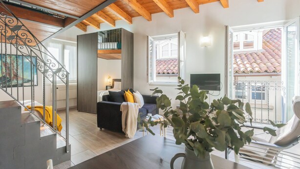 A modern living room with a wooden ceiling, a staircase, a sofa with cushions, a dining table, and a potted plant. - Domus 4 in Como by Rent All Como (Como)