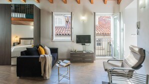 A modern interior with a wooden ceiling, a balcony with a tiled roof, a sofa, a chair, and a TV on a stand. - Domus 4 in Como by Rent All Como (Como)