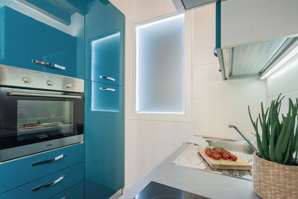 A modern kitchen with blue cabinets, a stainless steel oven, a window with frosted glass, and a potted plant. - Domus in Como by Rent All Como (Como)