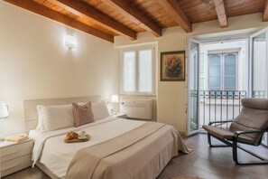 A bedroom with a bed, bedside table, lamp, and a chair near a window with a balcony. - Domus in Como by Rent All Como (Como)