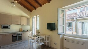 A modern kitchen with white cabinets, a dining table with chairs, a built-in oven, and a television mounted on the wall. - Domus 3 in Como by Rent All Como (Como)