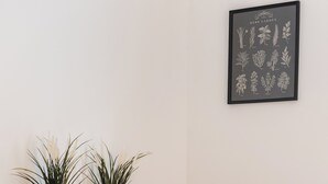 Una stanza con un letto, un tavolo da pranzo con sedie, due piante in vaso e una stampa botanica incorniciata appesa al muro.