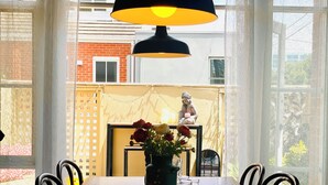Un comedor con una mesa larga, sillas, un florero con flores y una estatua de Buda.