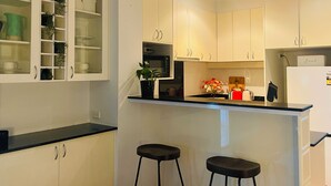 Una cocina moderna con armarios blancos, una encimera negra y dos taburetes negros.