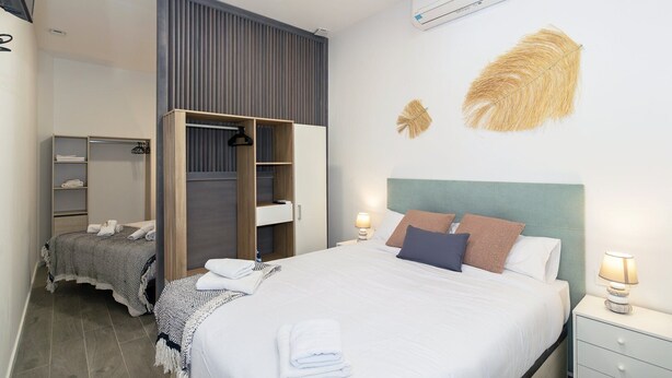 A modern bedroom with a bed, bedside tables, a wardrobe, and an air conditioning unit.