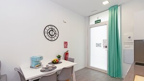 A small, modern room with a white table, two chairs, a clock, a fire extinguisher, and a door marked "SALIDA".