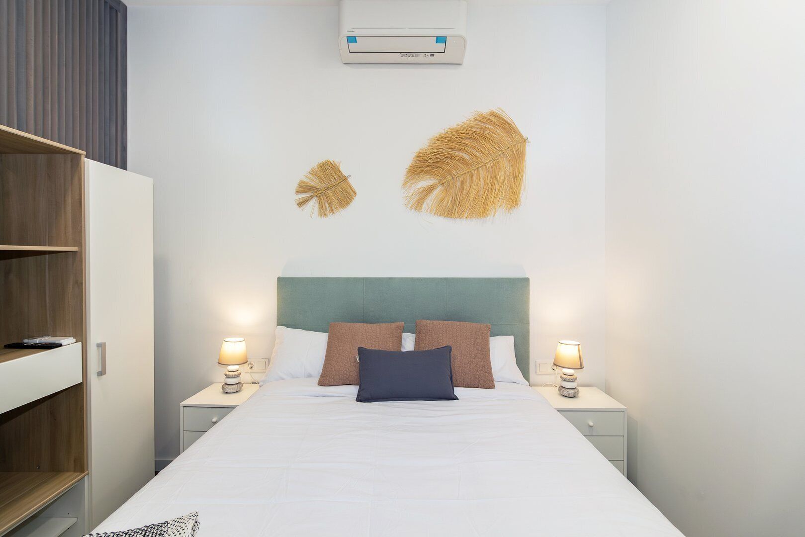 Une chambre d’hôtel moderne équipée d’un lit, de deux tables de chevet, d’une armoire et d’un climatiseur fixé au mur.
