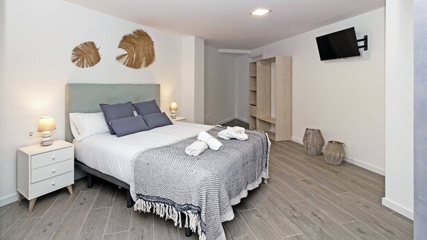 Une chambre à coucher moderne avec un lit, des tables de chevet, un téléviseur et une armoire en bois.