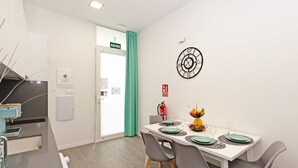 Un coin repas avec une table blanche, des chaises grises et une horloge au mur.