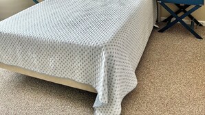 Une chambre à coucher comprenant un lit, deux tables de chevet, un ventilateur de plafond et un tableau accroché au mur.