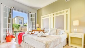 A bedroom with a large bed, a bedside table, a nightstand, and a window with a view of the outside.