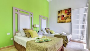 A hotel room with two beds, a green wall, a large window, and a painting.