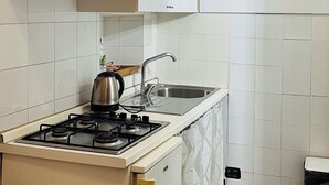 Kompakti keittiö, jossa on valkoiset kaapit, kaasuliesi, pesuallas ja pieni työtaso.