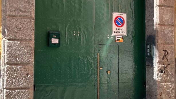 Vihreä metalliovi, jossa on pysäköintikielto-opaste, postilaatikko ja rekisterikilpi kiinnitettynä rakennuksen seinään.