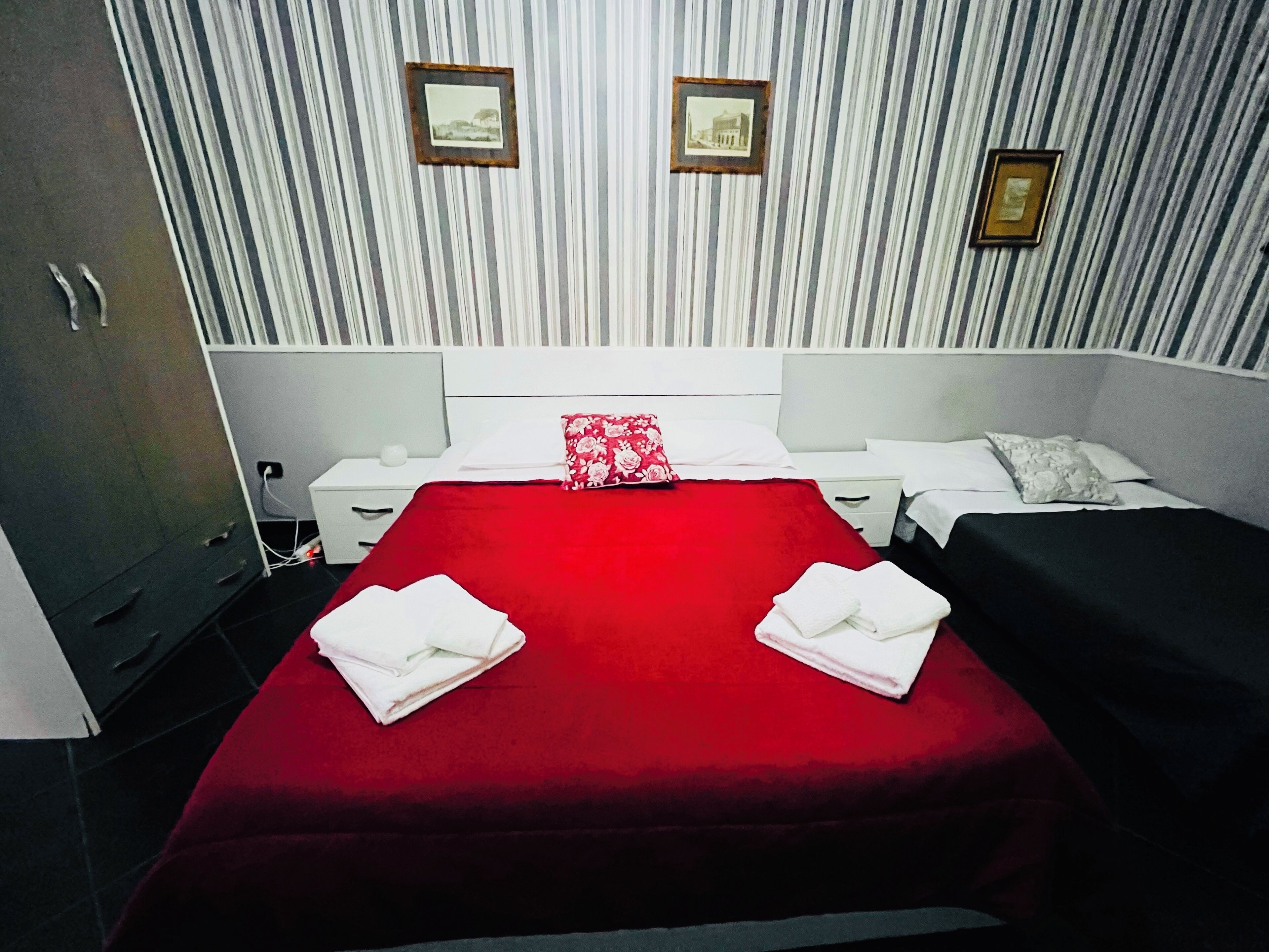 A hotel room with a large bed, two bedside tables, a wardrobe, and striped wallpaper.