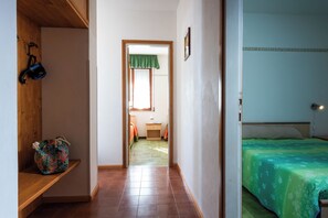 A narrow hallway leading to a bedroom with a bed, a small table, and a chair.