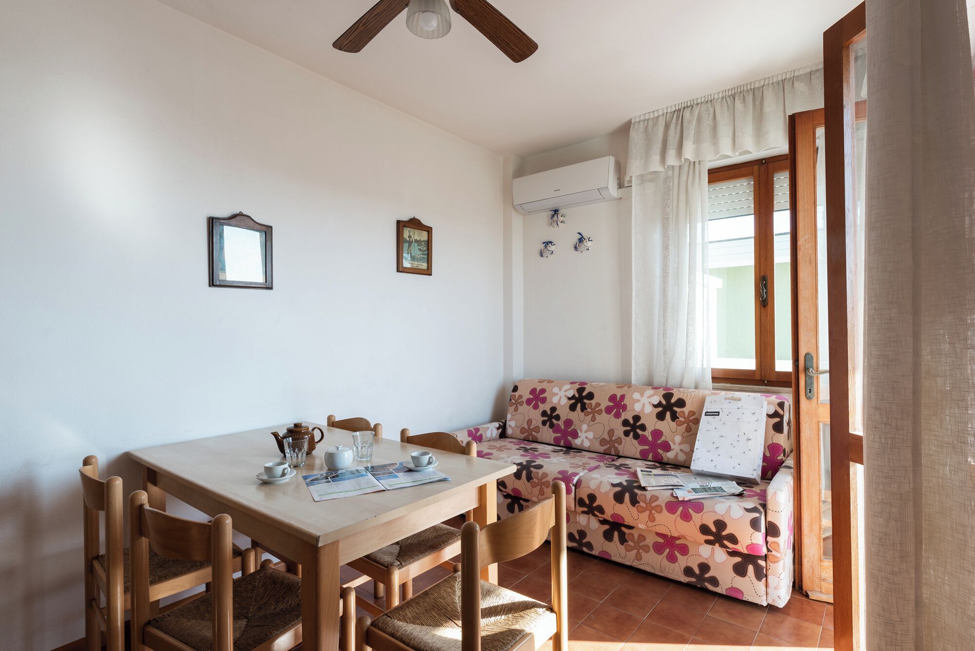 Una habitación acogedora con una mesa de comedor de madera, sillas, un sofá floral y un ventilador de techo.
