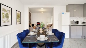 Un coin repas avec une table en verre, des chaises en velours bleu et un réfrigérateur blanc en arrière-plan.