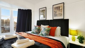Une chambre d’hôtel avec un grand lit, une table de chevet avec une lampe et deux tableaux encadrés au mur.