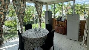 A dining area with a round table, black chairs, a ceiling fan, and large windows with patterned curtains.