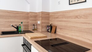 Una cucina moderna con piano cottura a induzione nero, un piano di lavoro in legno, lavastoviglie integrata e schienale in legno.