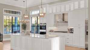 A modern kitchen with white cabinetry, a large island, pendant lighting, and a view of the outdoors.