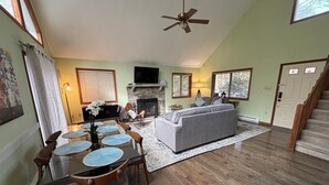 A living room with a fireplace, a sofa, a dining table with chairs, and a ceiling fan.