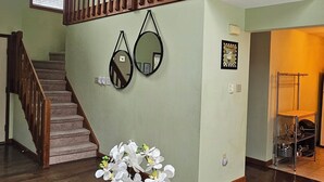 A spacious room with a wooden staircase, a dining area with round tables, and a wall-mounted mirror.