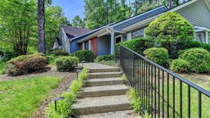 Ein Wohnhaus mit Veranda, einer Treppe zum Eingang und einem gepflegten Garten mit verschiedenen Sträuchern und Bäumen.