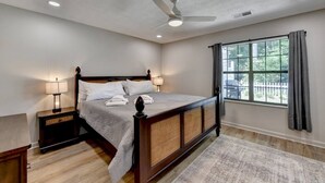 Ein Schlafzimmer mit Bett, Nachttischen, Deckenventilator, Fenster mit Vorhängen und Blick nach draußen.