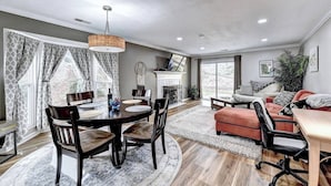 A spacious living room with a fireplace, a dining area with a round table and chairs, and a cozy seating area with a sofa and armchairs. - "Porchlight Stay" Single story duplex. Dine in downtown Alpharetta/shop Avalon (Alpharetta)