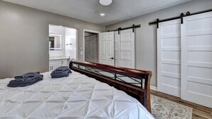 A bedroom with a bed, a ceiling fan, a large mirror, and a wardrobe. - "Porchlight Stay" Single story duplex. Dine in downtown Alpharetta/shop Avalon (Alpharetta)