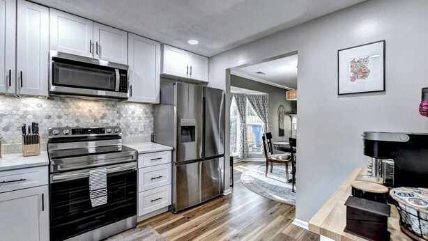 A modern kitchen with stainless steel appliances, white cabinets, and a wooden floor. - "Porchlight Stay" Single story duplex. Dine in downtown Alpharetta/shop Avalon (Alpharetta)