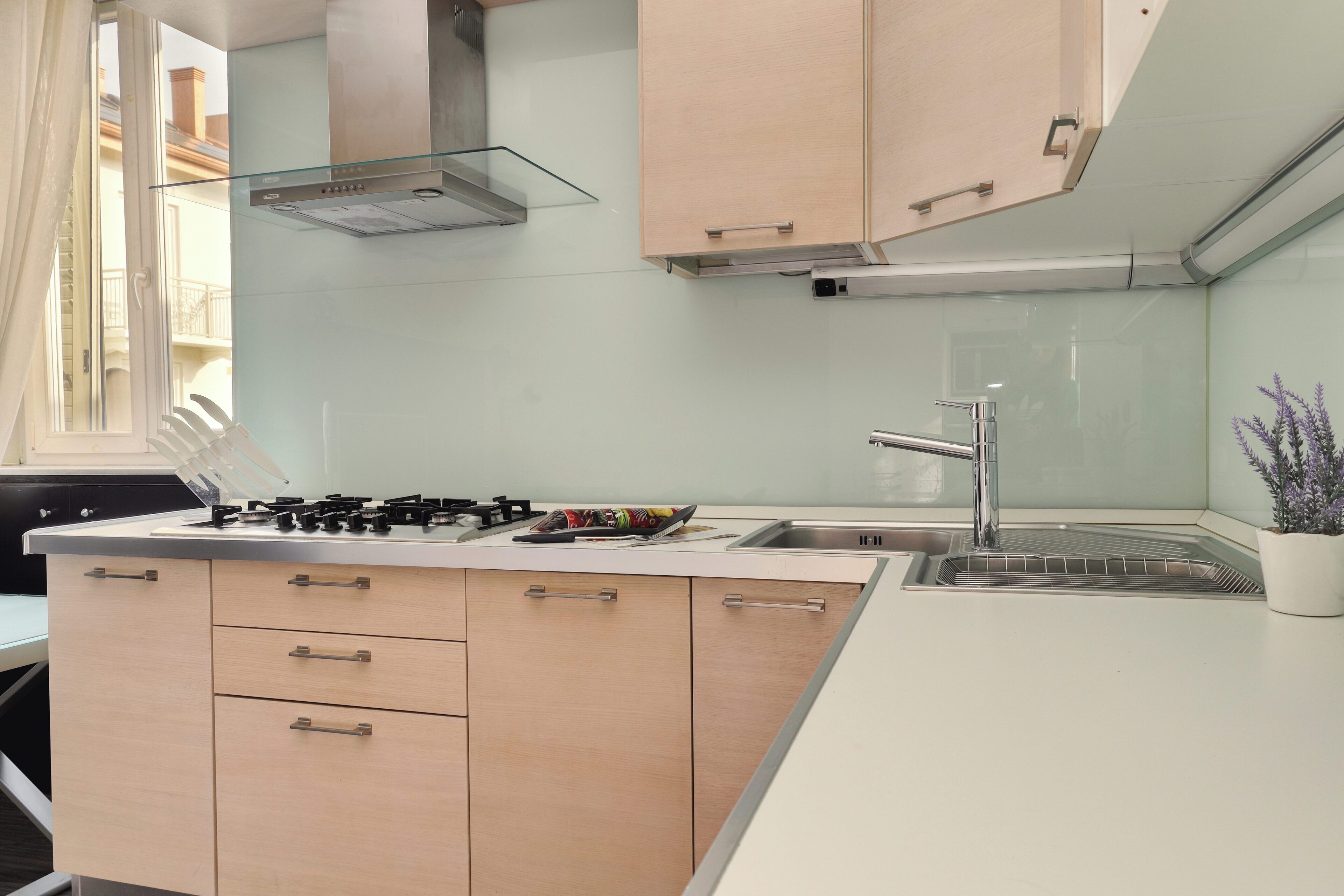 Una cocina moderna con estufa a gas, pileta de acero inoxidable y muebles de color claro.