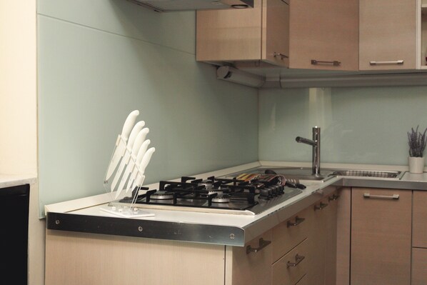 A kitchen with a gas stove, white cabinets, and a stainless steel sink.