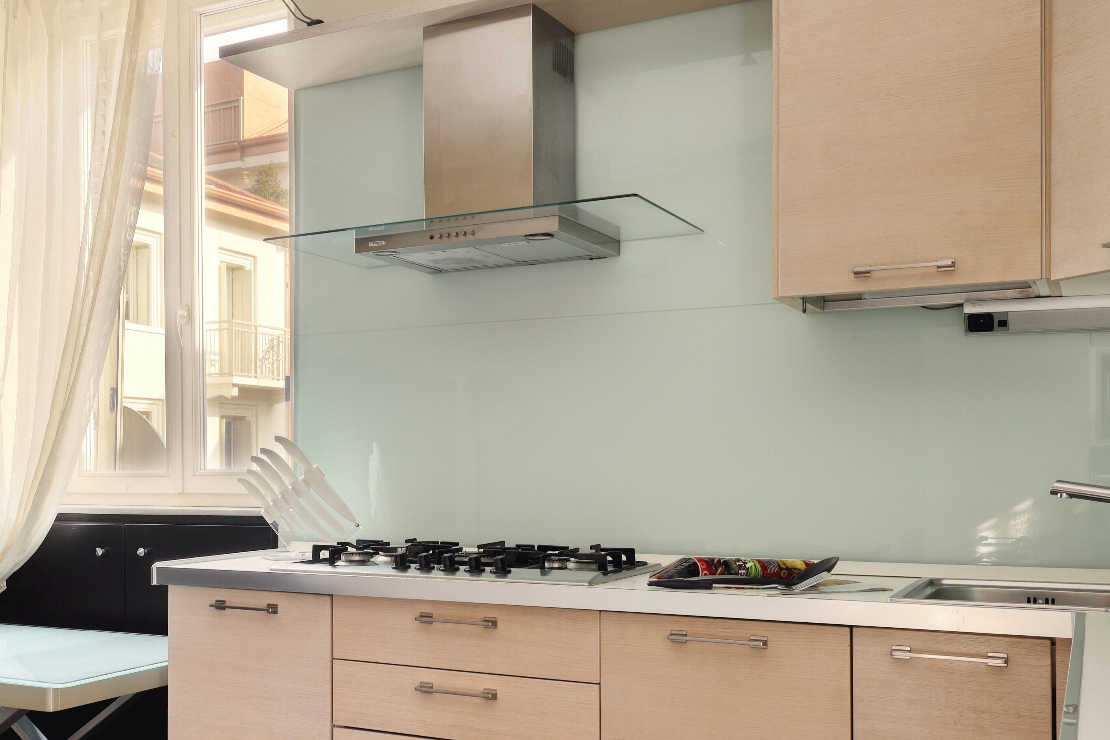 Une cuisine moderne équipée d’une cuisinière à gaz, d’une hotte en verre et de meubles de couleur claire.
