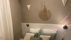 A neatly made bed with a white and beige bedspread, two pillows with geometric patterns, and a decorative woven piece on the wall.