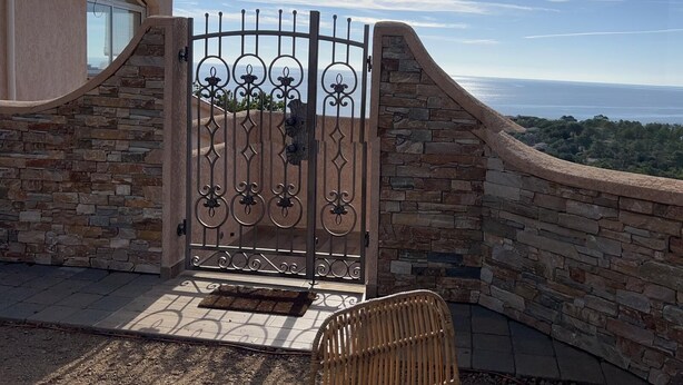 A gated entrance with a stone wall and a view of the ocean.