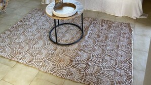 A cozy room with a white sofa, a round table with a woven top, and a patterned rug.