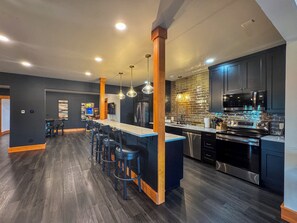Una cocina moderna con armarios oscuros, electrodomésticos de acero inoxidable y una isla central con taburetes de bar.