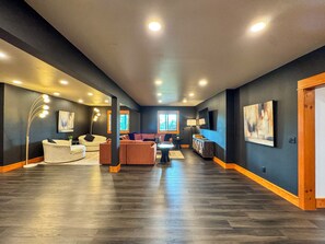A spacious living area with dark walls, multiple seating options, and a large window providing natural light.