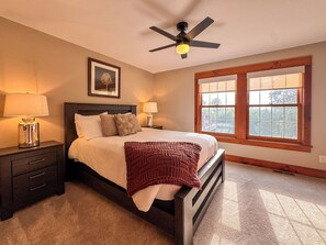 A bedroom with a bed, two bedside tables, a ceiling fan, a window, and a framed picture on the wall.