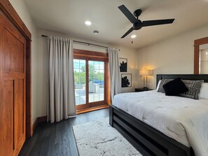 Un dormitorio con una cama, un ventilador de techo, una mesita de noche, una lámpara y vistas a través de una ventana.