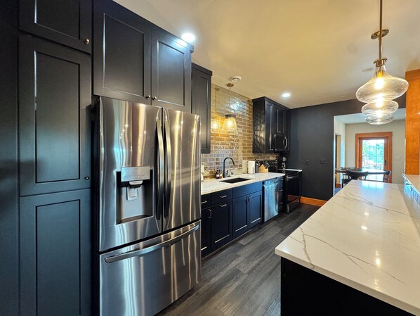 A modern kitchen with stainless steel appliances, dark cabinetry, and a marble countertop.