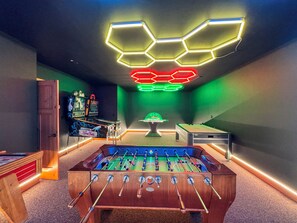Una habitación con mesa de futbolín, mesa de billar y luces de neón en el techo.